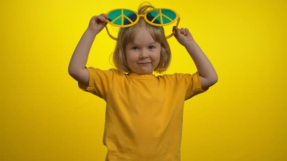 Sweet Little Girl in Funny Yellow Hippie Sunglasses is Looking at the Camera