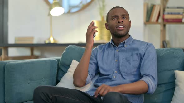 Young African Man Talking on Smartphone on Sofa 