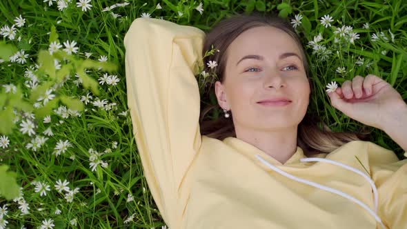 Beautiful Young Woman Lying on the Grass Against the Background of Flowers in the Forest