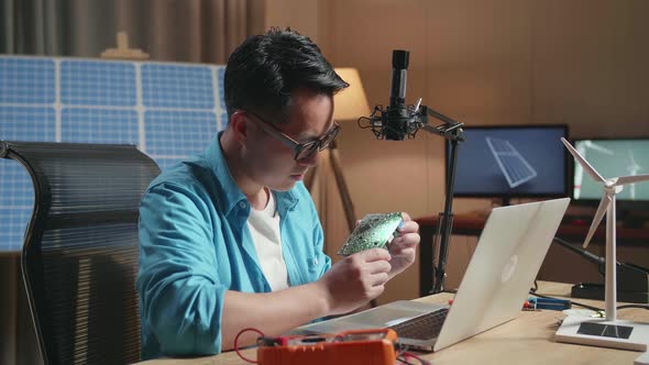 Man With Wind Turbine Looking At Circuit Board While Working With Laptop Next To The Solar Cell