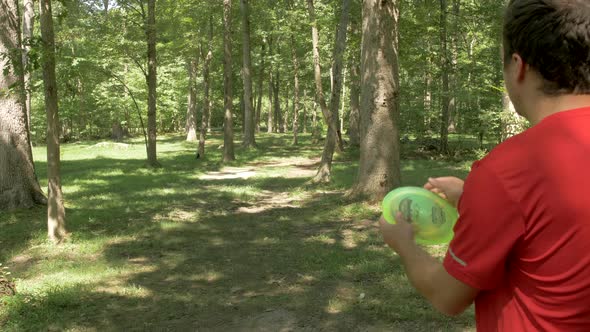 A Man Starts a Round of Disc Golf with an Impressive Drive Through Trees in Slow Motion