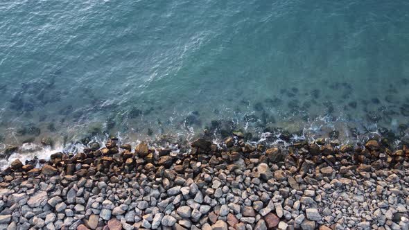 Shore with stones washing the waves of the blue sea.