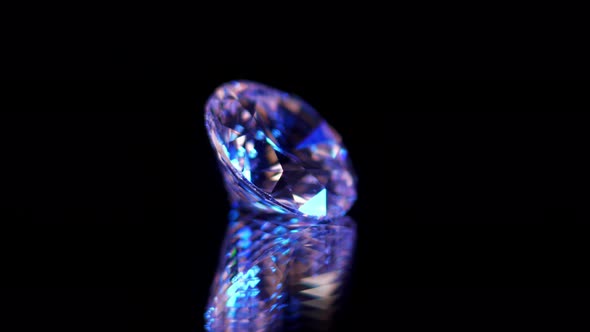 Macro shot of high quality diamond isolated on black relfecting surface, illuminated by purple and b