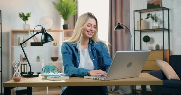 Modern Blond Young Woman Sitting at the Desk at Home and Chatting with Friends on Computer