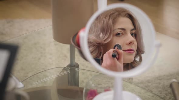 Reflection of Beautiful Caucasian Girl Applying Face Powder. Focus Changes From Mirror To Makeup Set