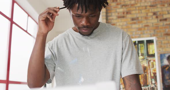 African american male painter holding brush and thinking in artist studio