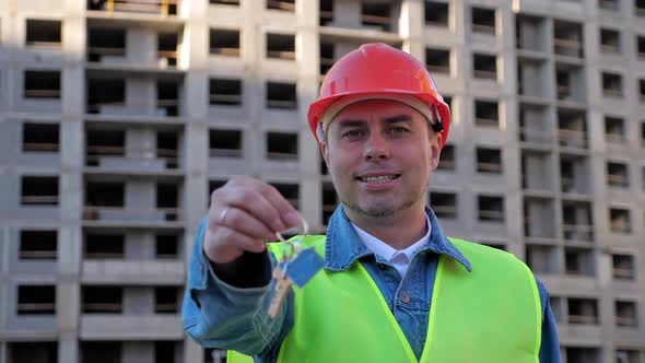 Worker in Yellow Protective Helmet Show Key at Construction Site