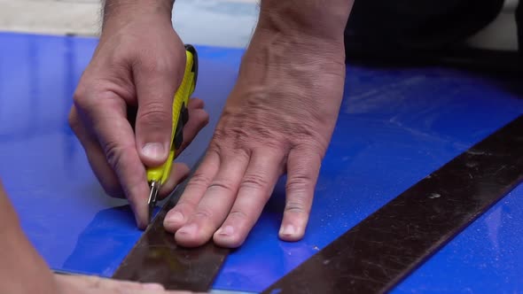 A builder cuts a sheet of blue plastic with a knife.