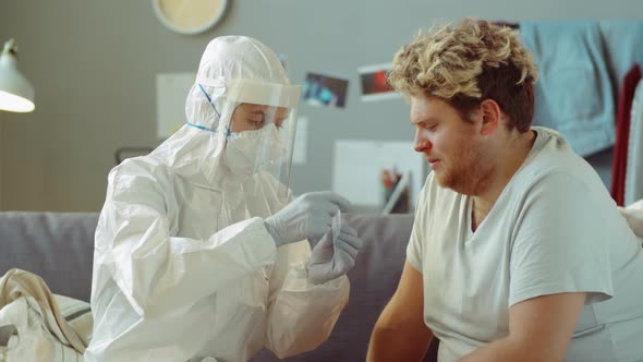 Doctor in Protective Suit Taking Nasal Swab from Man at Home