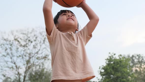 Cheerful cute girl playing basketball outdoors.