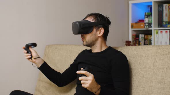 A man wearing VR glasses actively playing on the couch. In the background is a rack of games