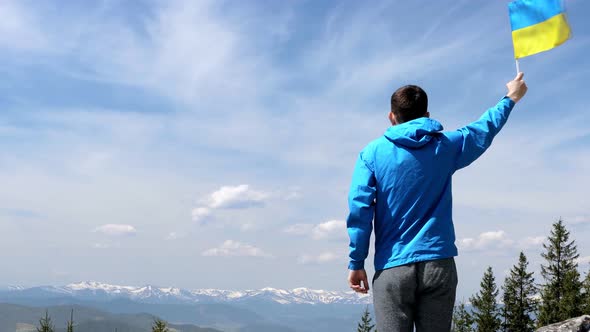 Patriot man waving Ukrainian flag on top of the mountain peak. Celebrating the victory of war.