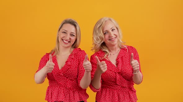 This is Excellent Two Blonde Caucasian Joyful Women Showing Thumbs Up Orange Background Medium Shot