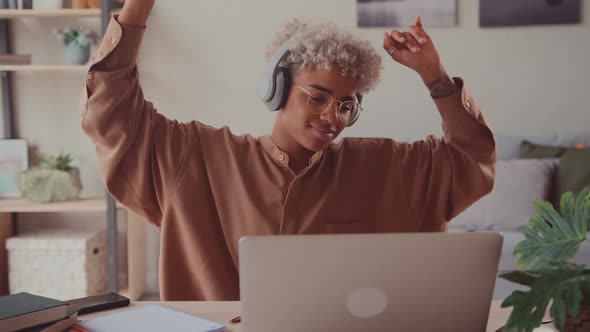 African Female Listening Music At Workplace Dancing In Headphones At Home Office