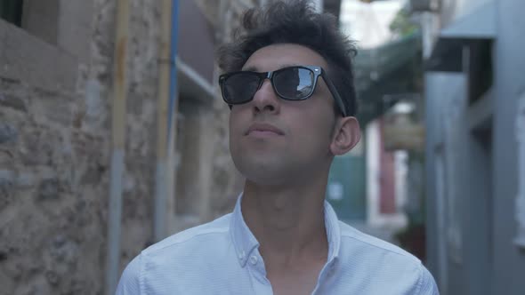 Young man looks around street wearing sunglasses