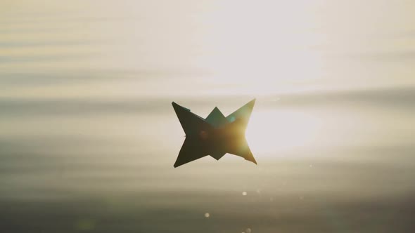 Paper boat floats alone with its reflection on the wavy water in the river at sunset.