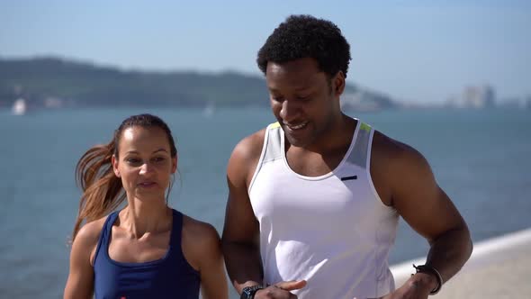 Multiethnic Couple in Sportswear Jogging Along Embankment