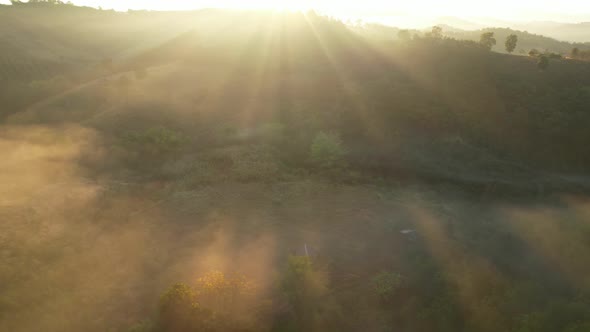 Aerial view of sunrise with fog above mountains. Golden hour and amazing sun rays. Nan, Thailand