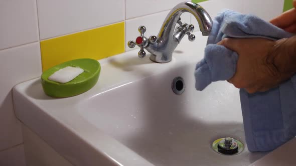 A man washes his hands, closes the faucet valve. Takes a blue towel and wipes his hands