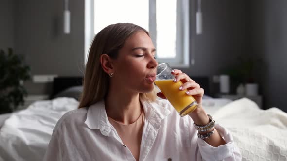 Smiling girl sits on floor in bedroom and drinking orange juice