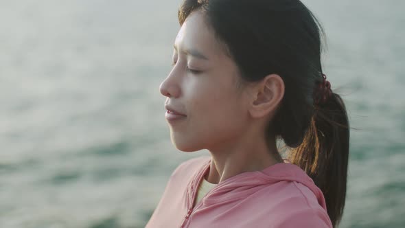 Portrait of young Asian woman relaxed enjoying peaceful sunset and looking up exhaling fresh air.