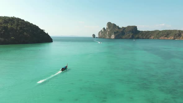 Long-Tail Boat sailing through idyllic emerald green sea in Loh Dalum Bay in Ko Phi Phi, Thailand