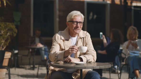 Aged Man Drinking Coffee and Flirting with Woman at Next Table in Outdoor Cafe.