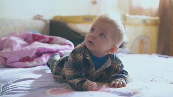 Little Baby in Warm Clothes Lies on Comfortable Bed in Room