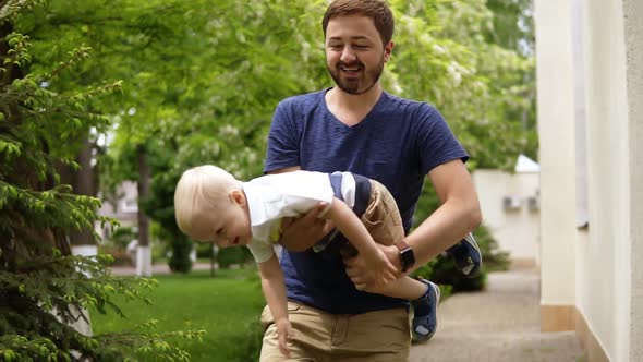 Father is Playing with His Little Blondy Son Outdoors