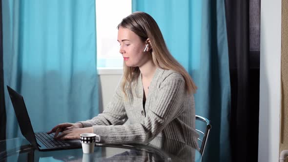 Young fair-haired woman is working on her laptop from home