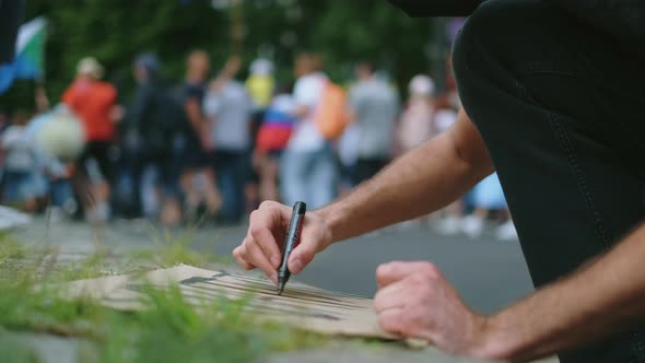 Male Protester Drawing Banner Sign in Hands with Marker in Rally Riot Crowd