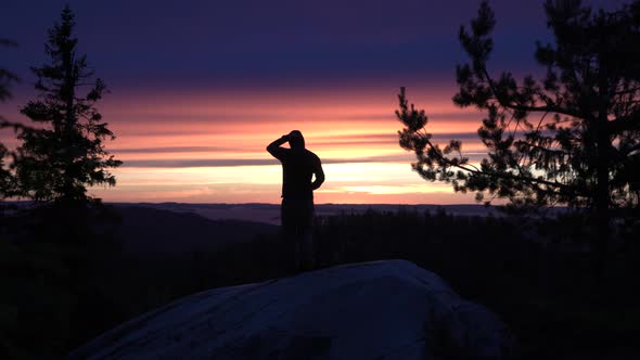 Silhouette of male hiker photographer standing on a nordic mountain cliff looking towards horizon wi