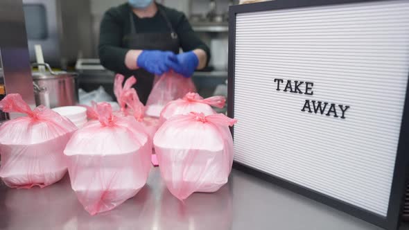 Closeup Take Away Message with Packed Food on Counter and Blurred Female Volunteer Working at