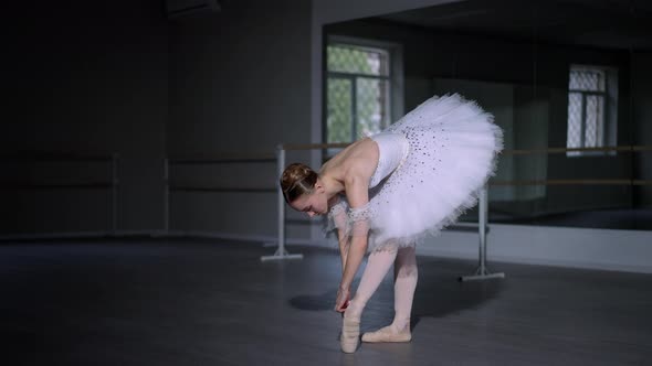 Portrait of Confident Slim Gorgeous Ballerina in White Dress Tying Lace on Pointe Shoes Standing in