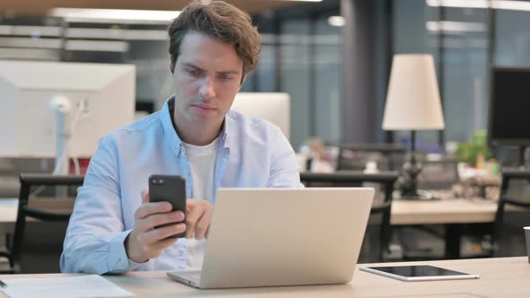 Man Using Smartphone While Using Laptop in Office