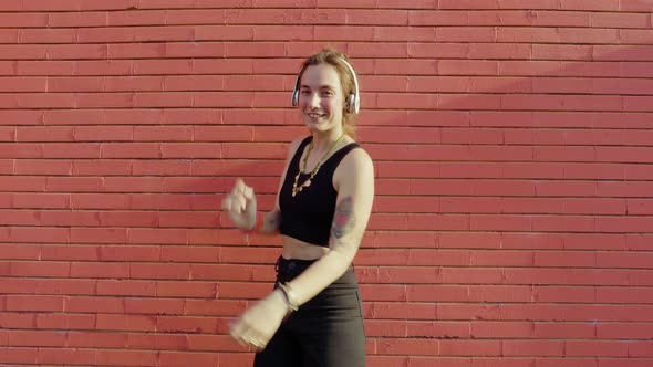 Young woman listening to music and dancing in front of red wall