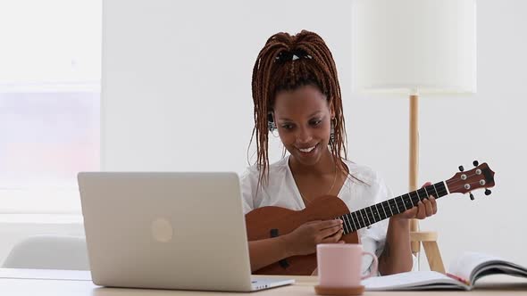 Young African American Woman is Learning to Play the Ukulele Guitar Using Laptop Computer Spbi