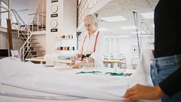 Woman Tailor of Sewing Workshop Drawing Pen Around Pattern Standing at Table Seamstress Spreading