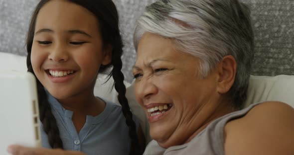 Grandmother and granddaughter using digital tablet in bed room 4k