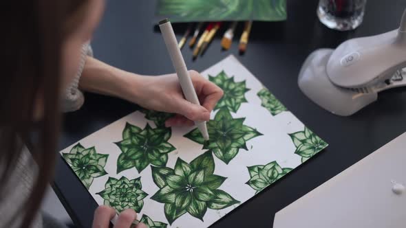 Top View Young Caucasian Woman Painting Green Leaves on Paper Sitting at Table Indoors