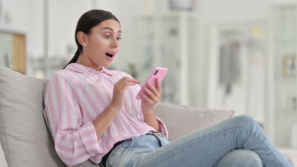 Excited Latin Woman Celebrating Success on Smartphone at Home