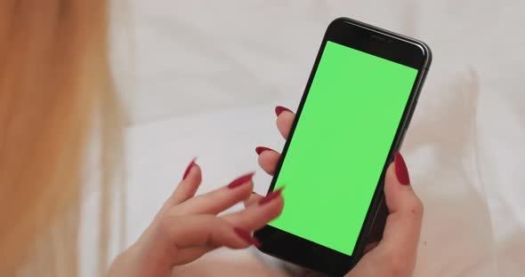 Woman Resting on Bed and Scrolling on Green Empty Screen of Modern Smartphone