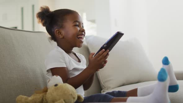 Happy african american girl lying on sofa watching tv at home