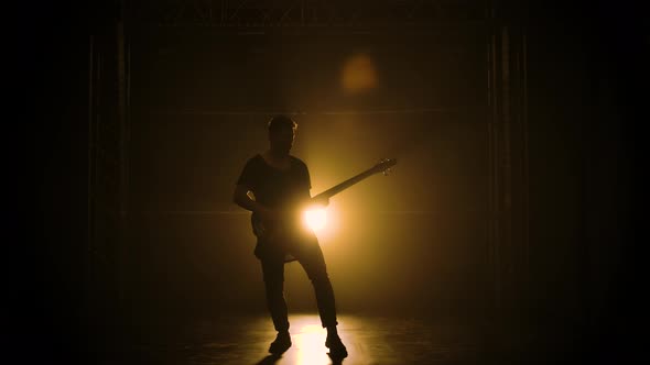 Silhouette of a Young Guy Playing on the Electric Guitar on Stage in a Dark Studio with Smoke 