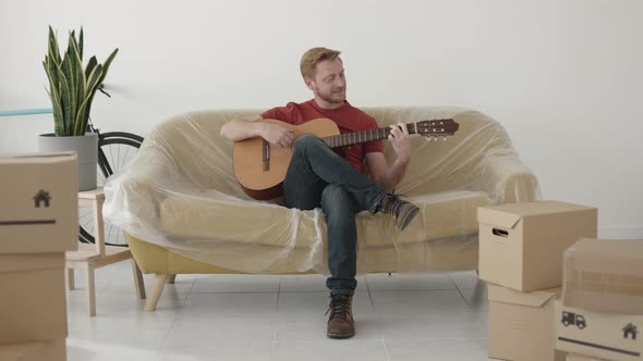 Cheerful Young Man Playing the Guitar at New Home