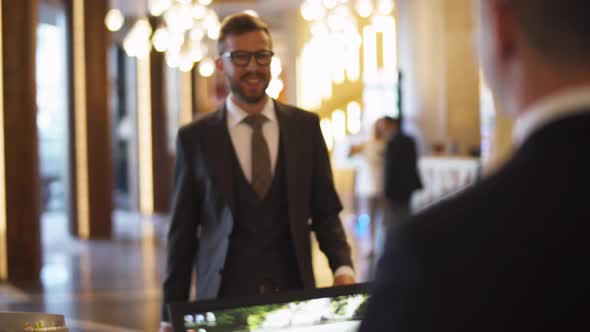 Businessman in Suit Carrying a Suitcase Man Goes To Reception of Hotel and Receives a Key Card From
