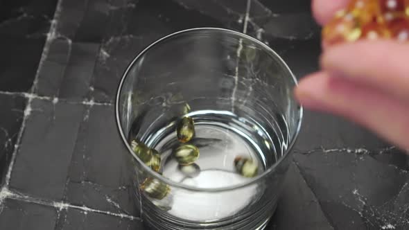 Omega 3 pills are falling from hands into a glass 