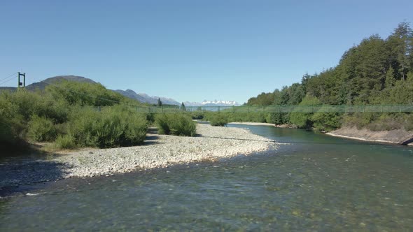 Aerial parallax of Rio Azul river and elevated bridge surrounded by trees and mountains, Patagonia A