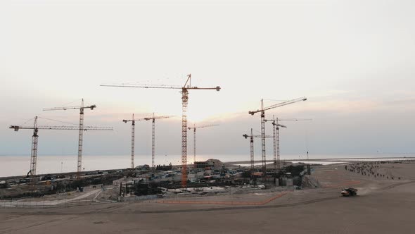 Aerial Drone Flying at a Construction Site, a Truck Is Driving Along the Road, a Crane Raises a Wall