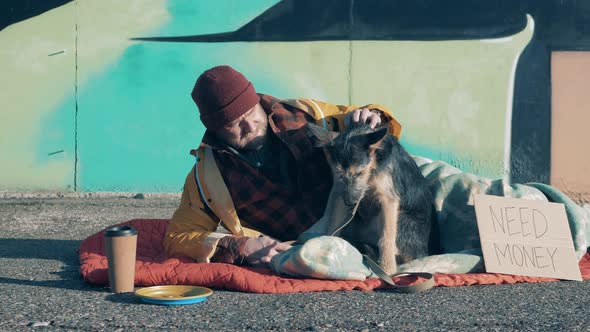 A Beggar and His Dog are Lying on the Ground Near a Graffiti Wall